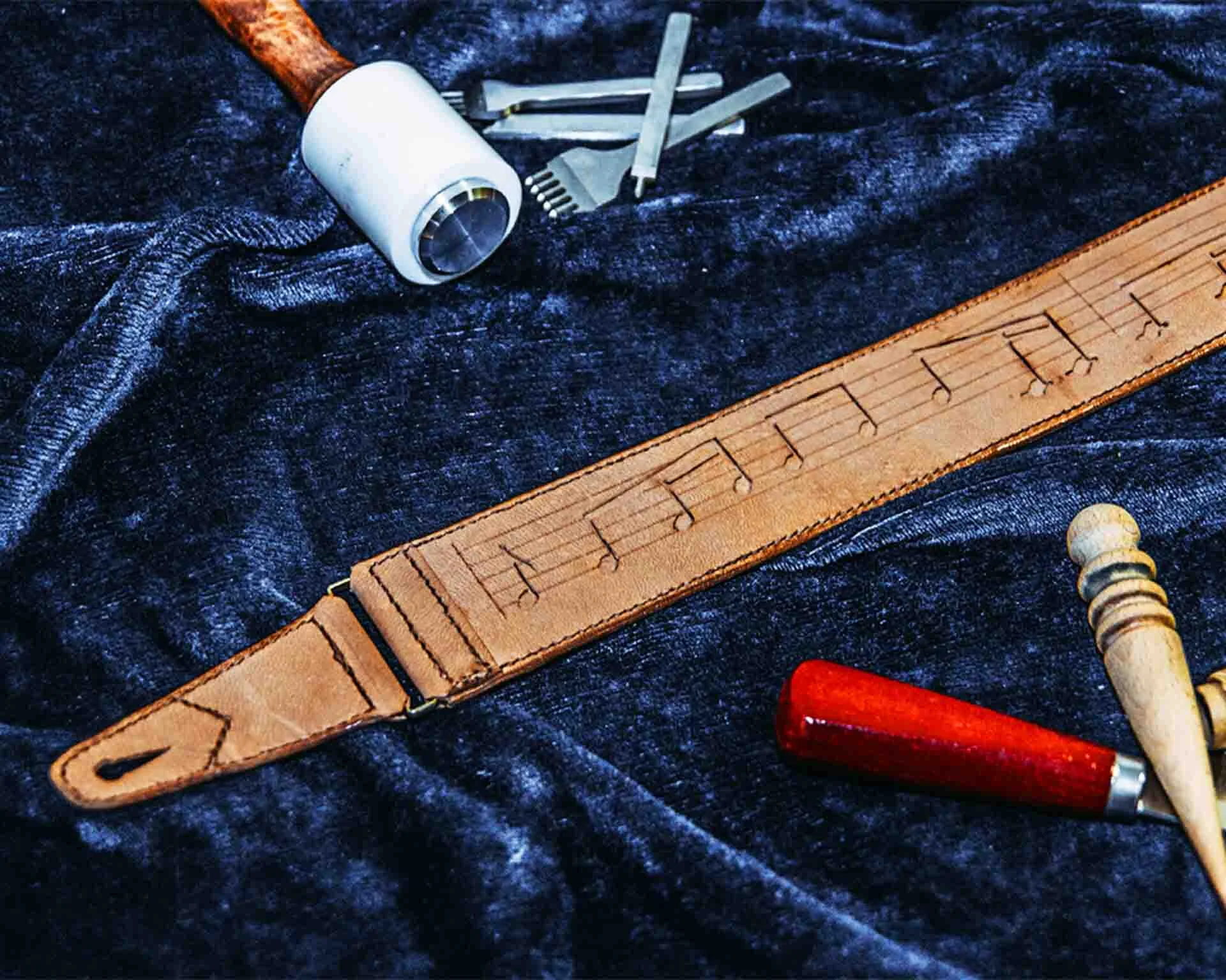 Product photo of leather guitar strap laid amongst tools such as stamps, hammers and a carving knife