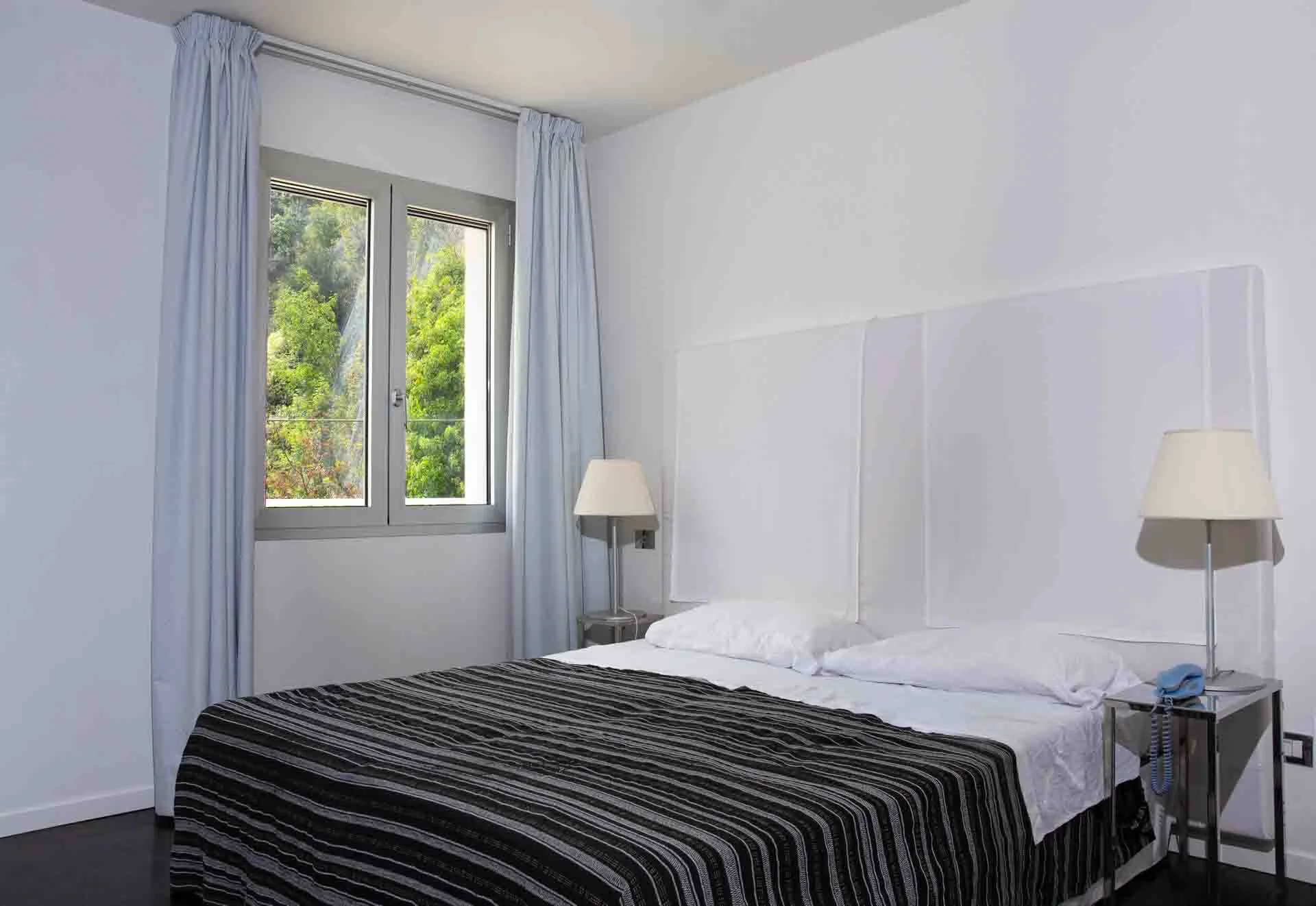 Small one-bed apartment room with coffee tables next to the bed and lamps on top